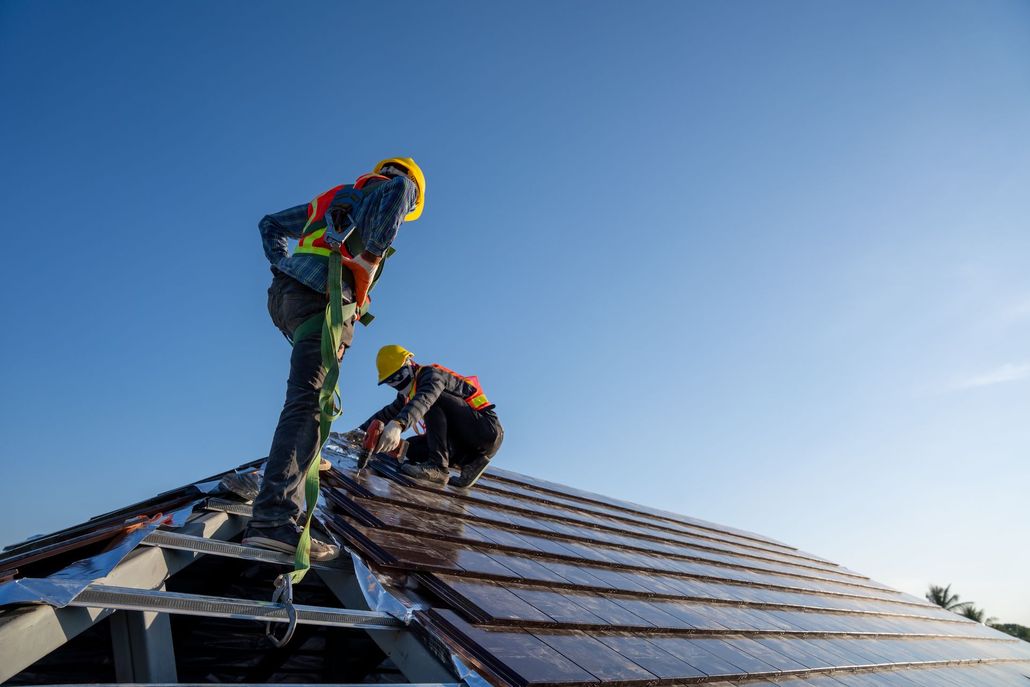 Two workers installing solar panels on a rooftop under a clear blue sky