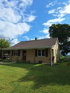 Single-story beige house with a porch and green lawn under a bright blue sky