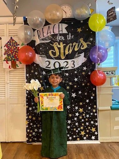 Child in green costume holding a certificate at a “Peace in the Stars 2023” school backdrop with balloons