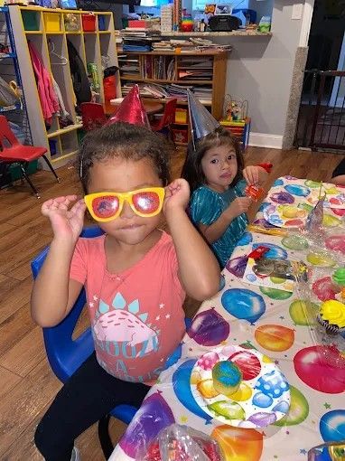 Child wearing pink sunglasses at a birthday party table with colorful plates, another child in the background