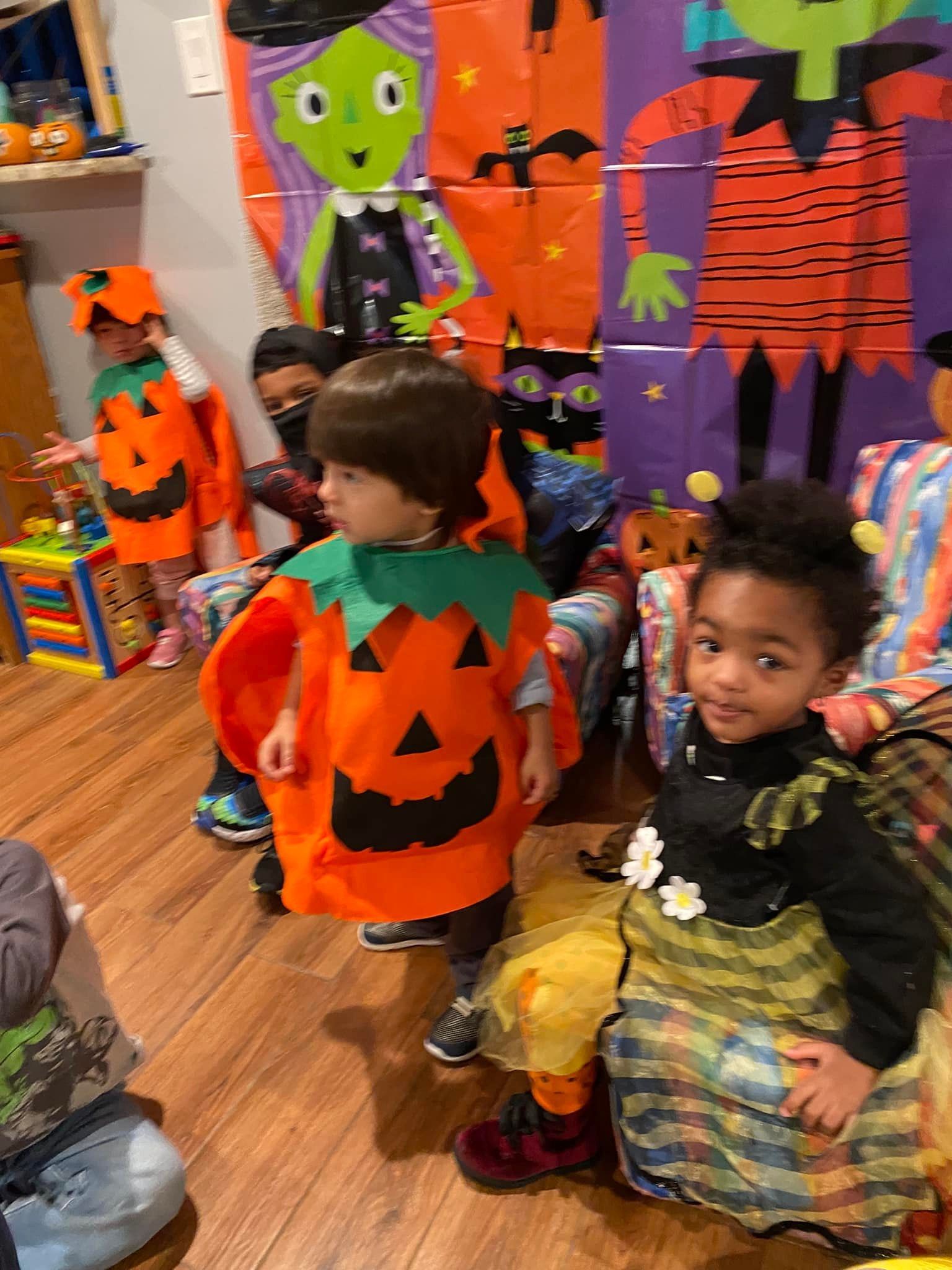 Two children in Halloween costumes stand in front of a spooky orange-and-purple Halloween display.