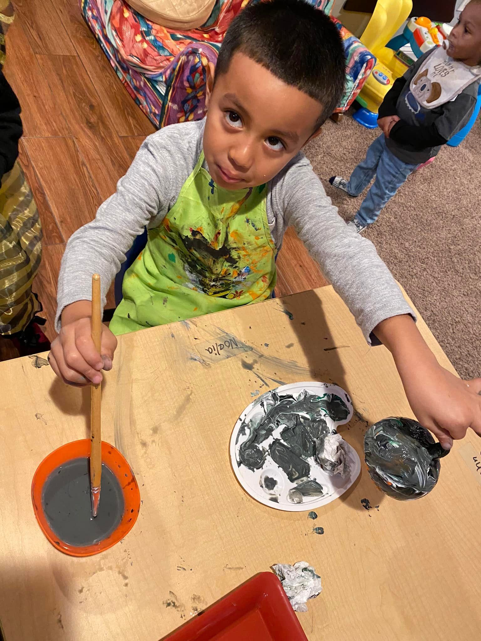Child painting at a table with orange, black, and white paint in a classroom setting