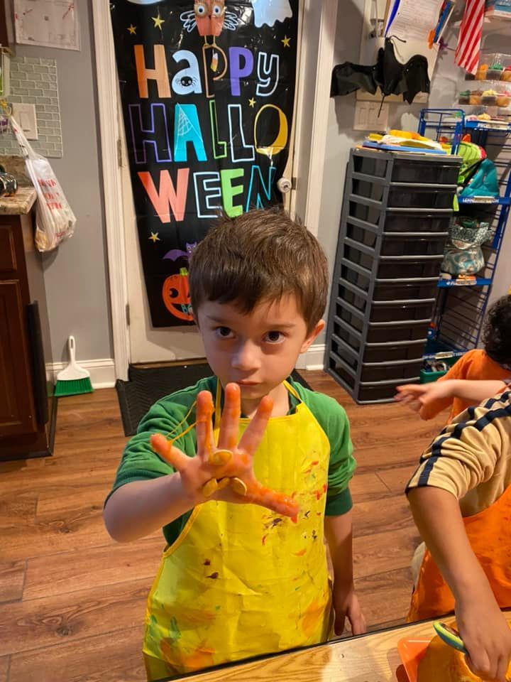 Child in a yellow painted shirt holding up a hand in a Halloween-decorated room