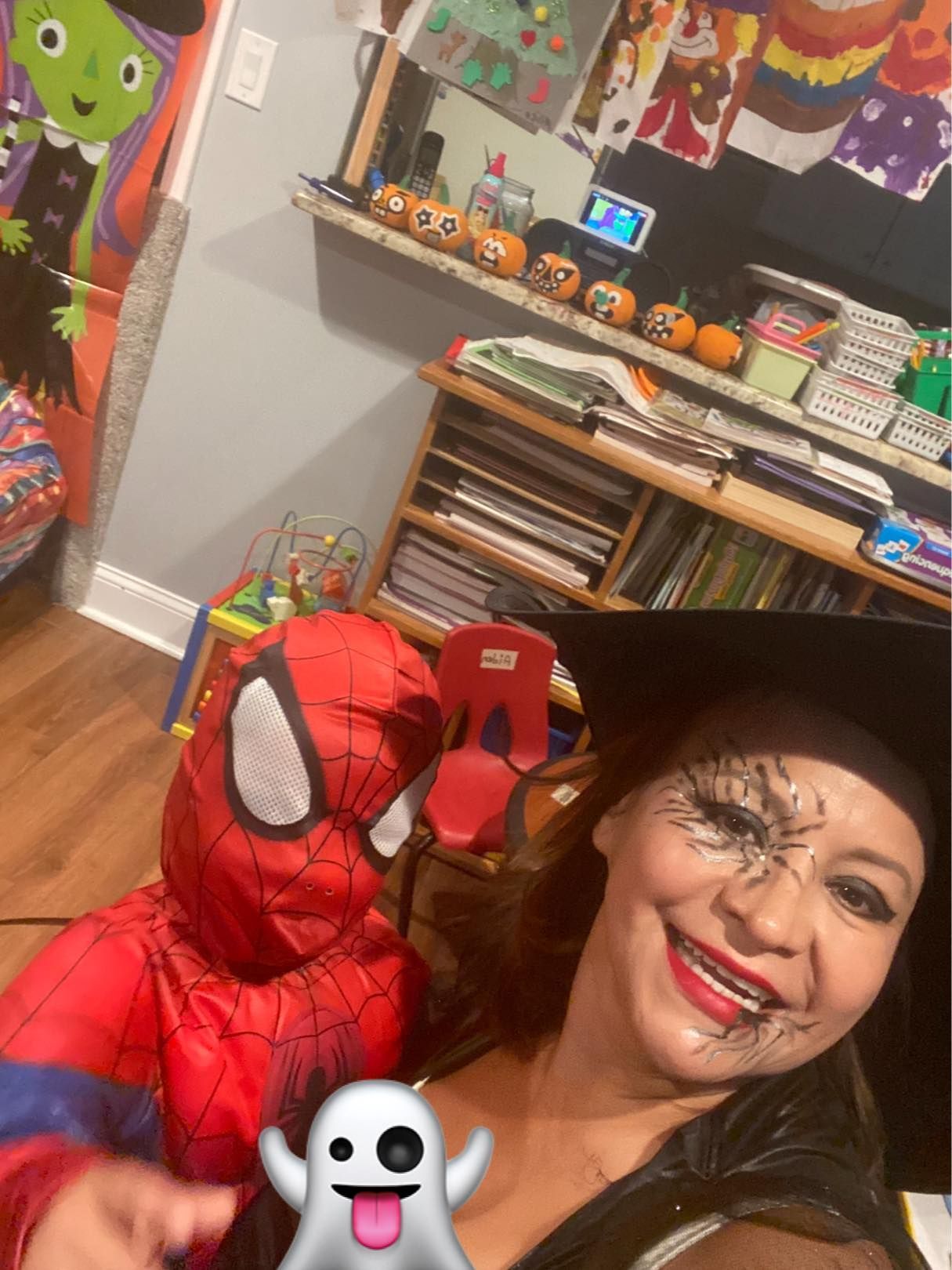 Person in a Spider-Man costume taking a smiling selfie in a decorated room with toys and shelves.