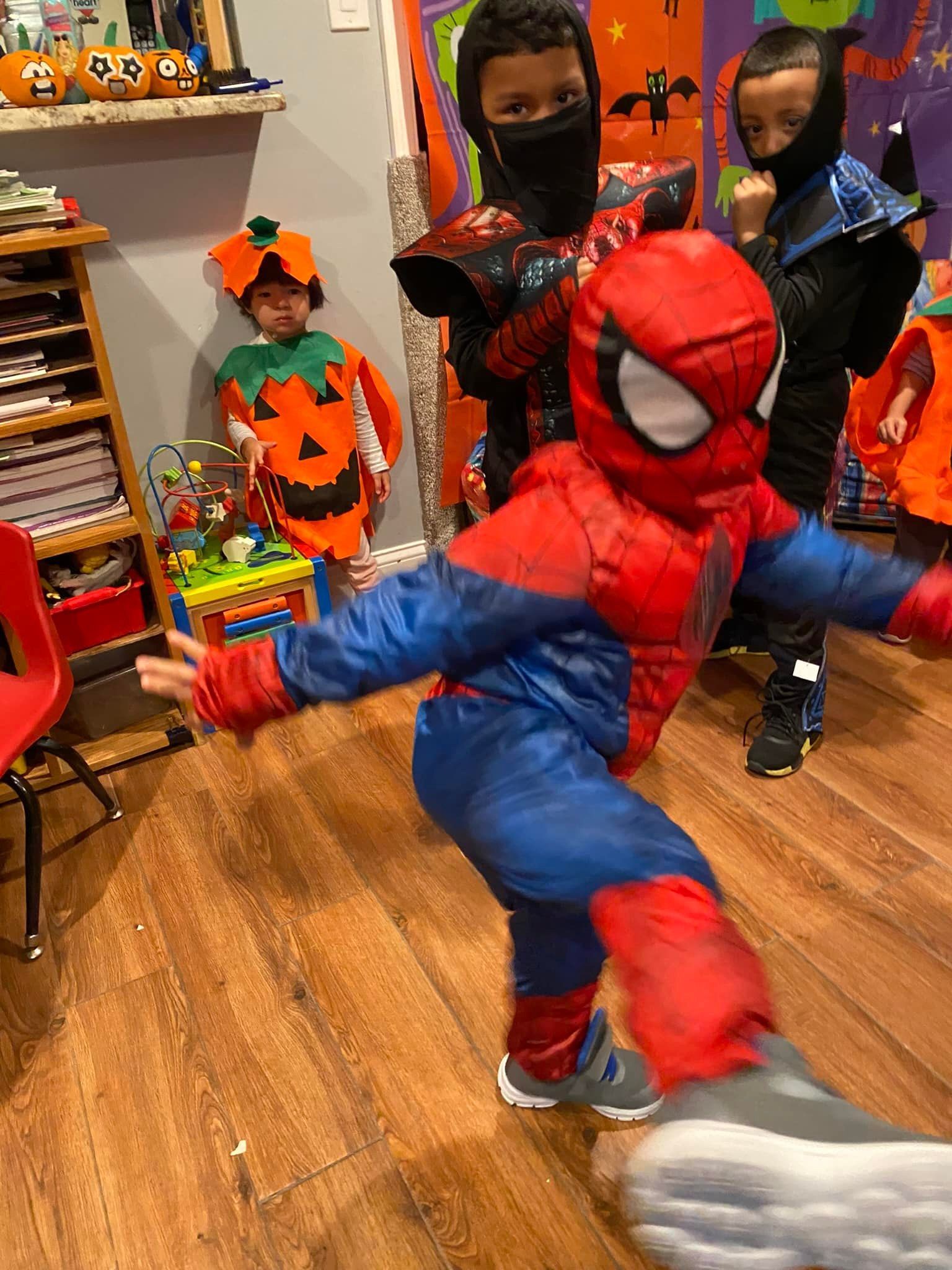 Child in Spider-Man costume posing in a playroom with other costumed children.