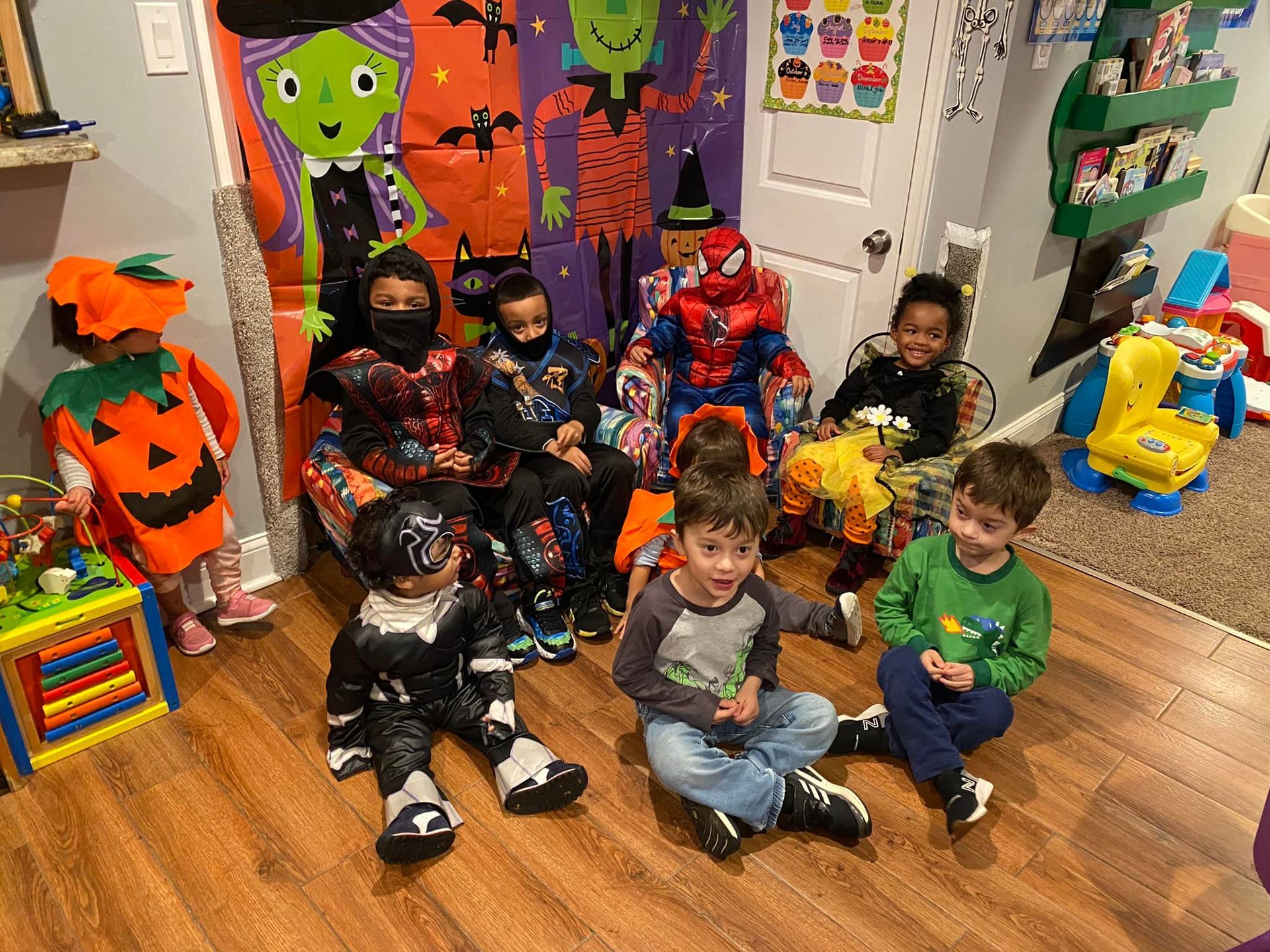 Children in costumes sitting on a classroom floor with Halloween decorations and pumpkins