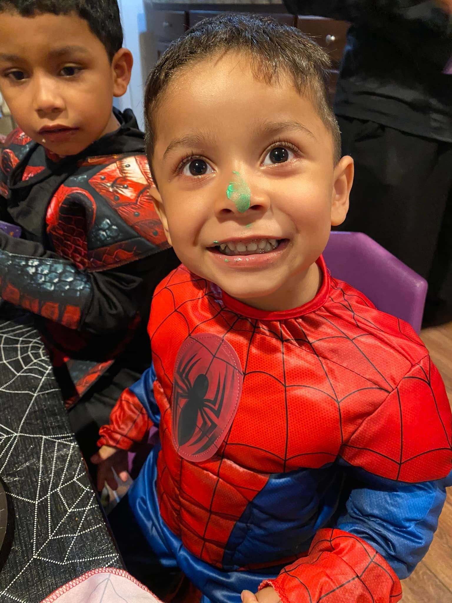 Two children in Spider-Man costumes smiling at a table, one close to the camera.
