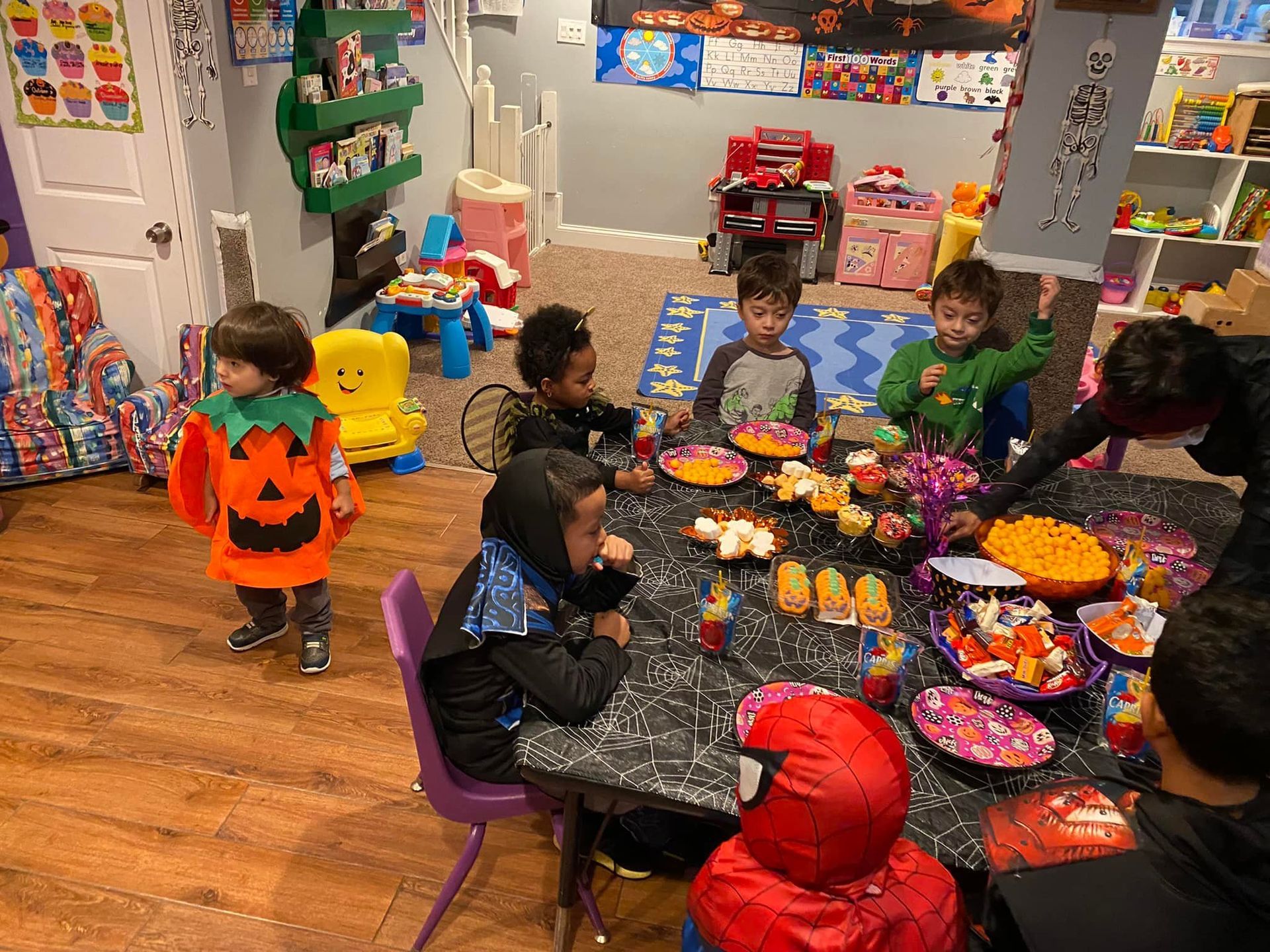 Children in costumes sit around a Halloween party table with treats and decorations.