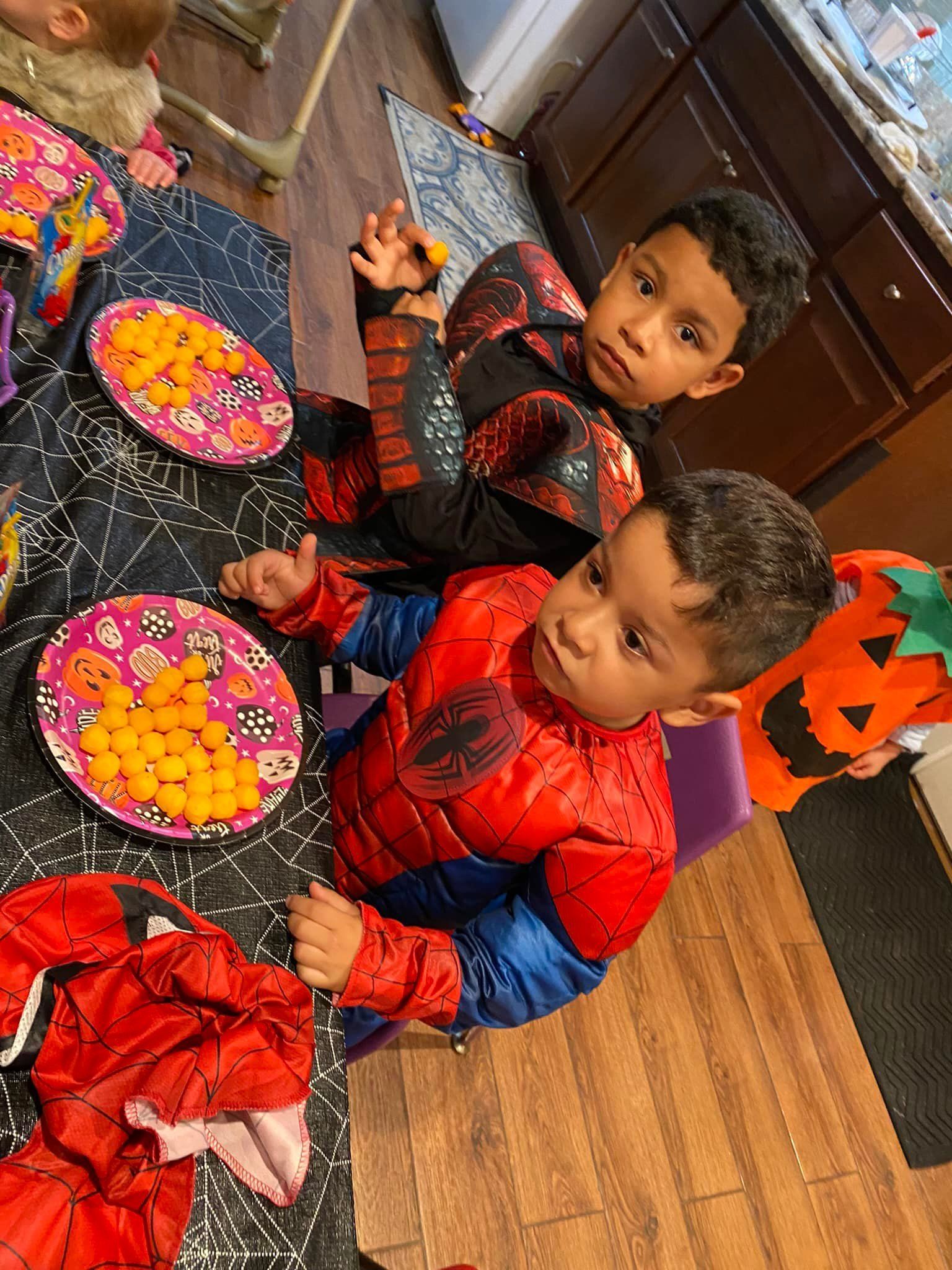 Two children in red and black clothing seated at a table with bowls of colorful flowers and orange decorations