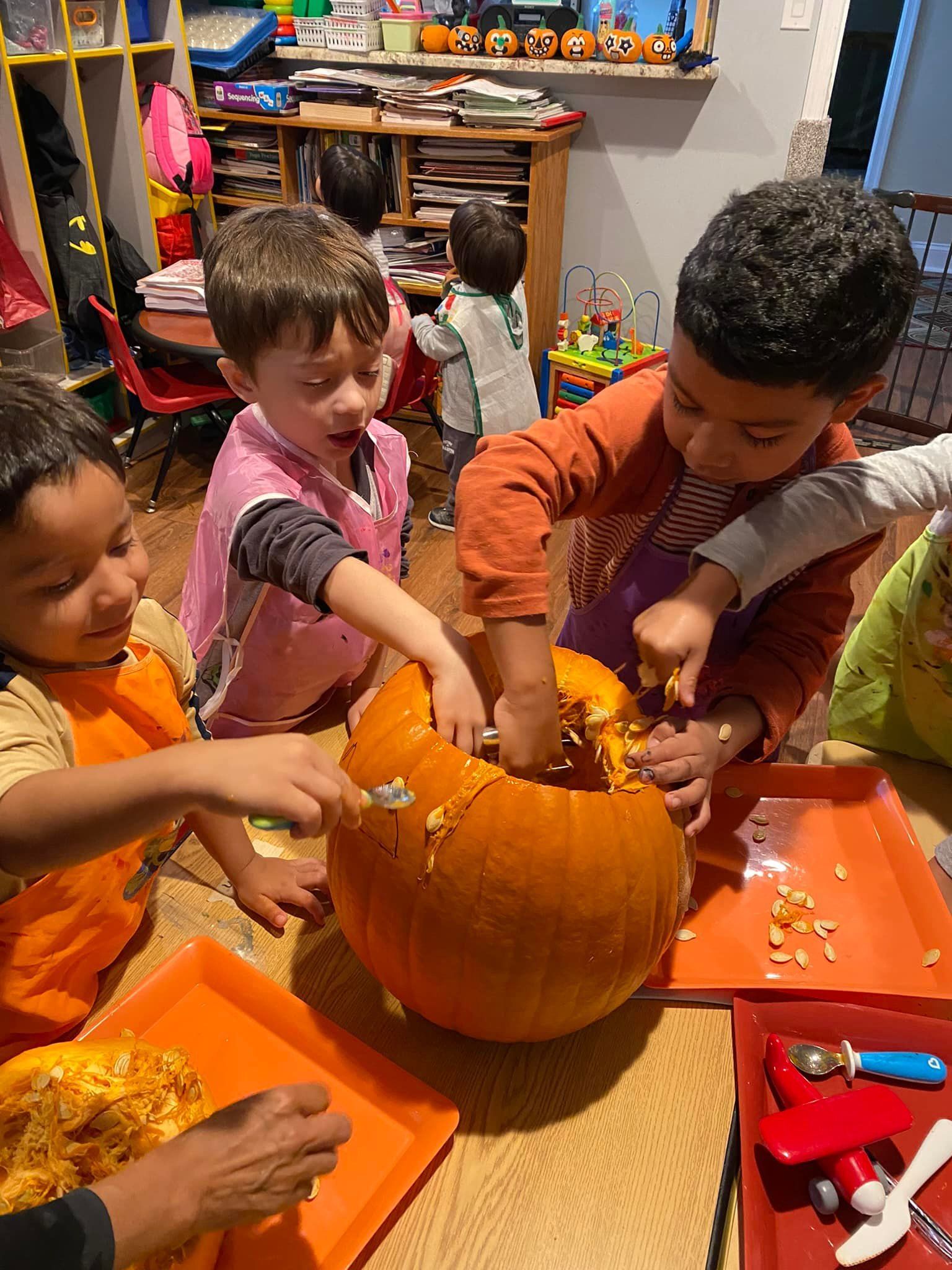 Children scooping seeds from a carved orange pumpkin at a table with Halloween decorations