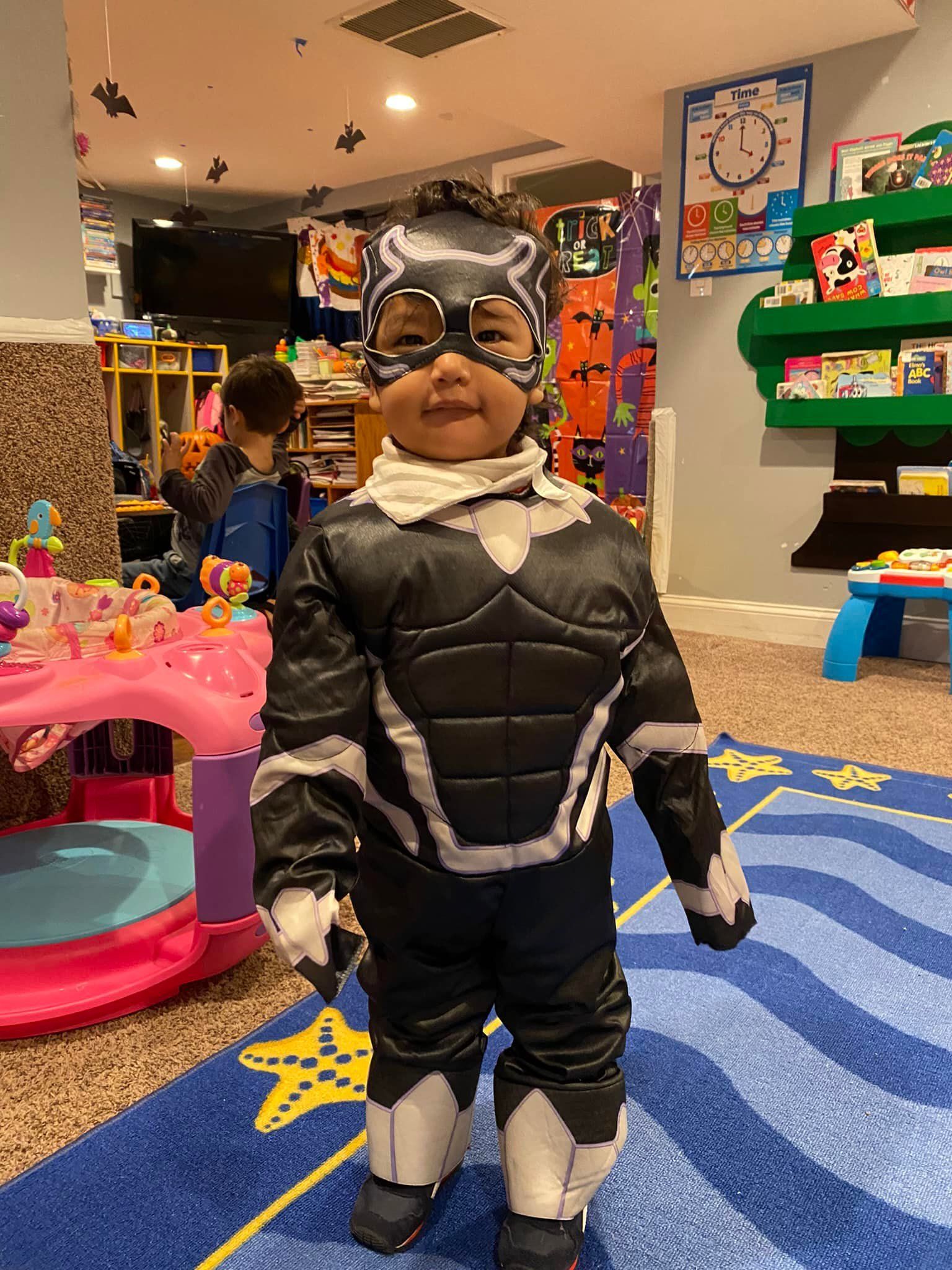Child in a Black Panther costume standing in a colorful indoor play area.