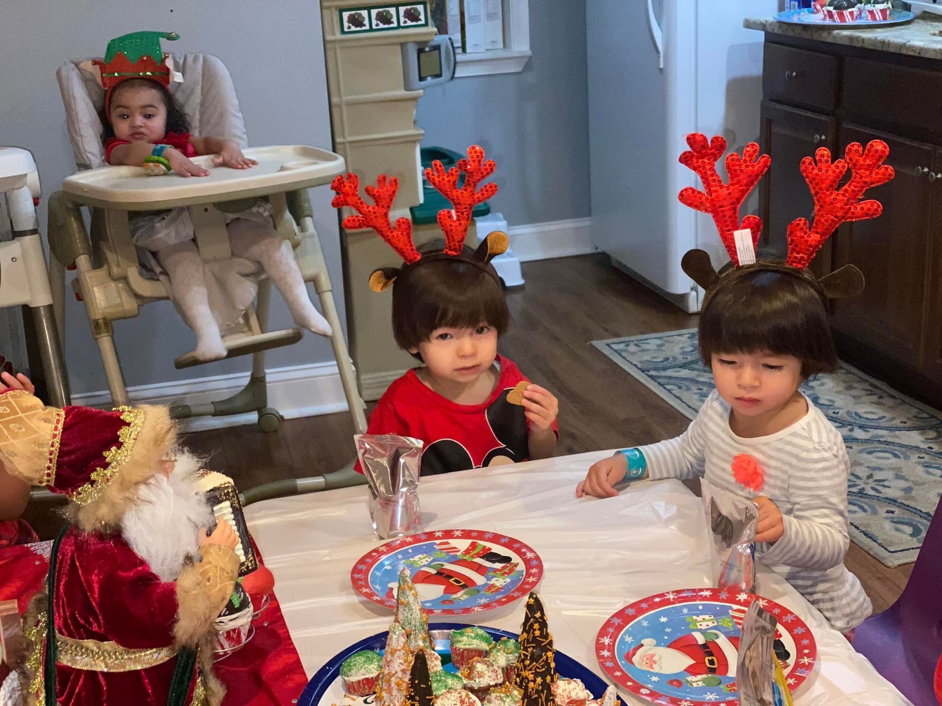 Children in festive antler headbands sit at a holiday table with games and snacks.