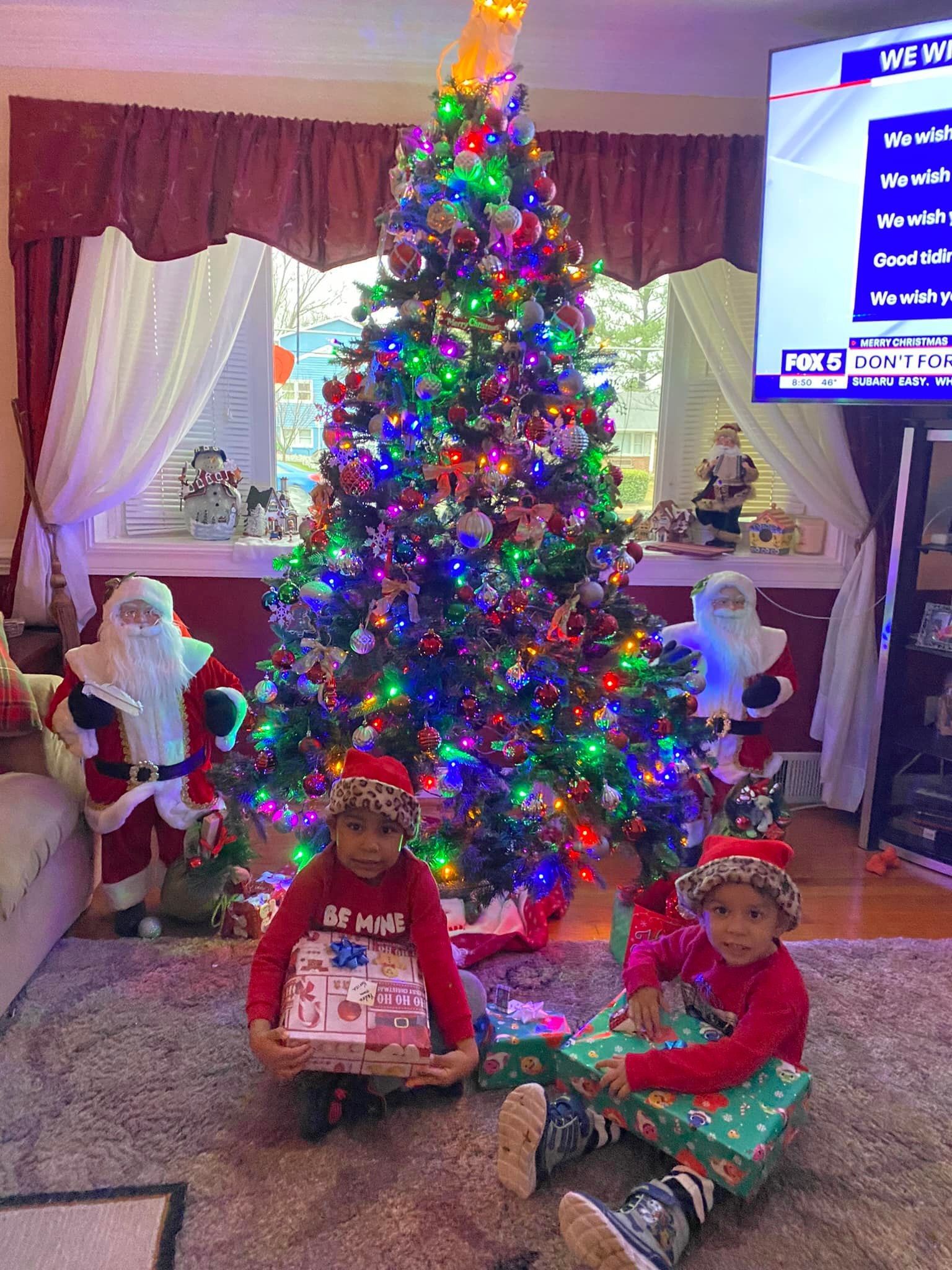 Children sitting in front of a decorated Christmas tree with Santa figures in a living room