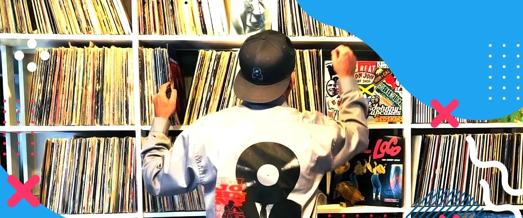A person wearing a cap stands before floor-to-ceiling shelves filled with vinyl records, reaching to select a disc.