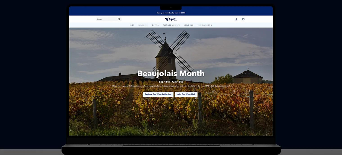 A laptop screen displaying a wine website homepage featuring a vineyard and windmill under a