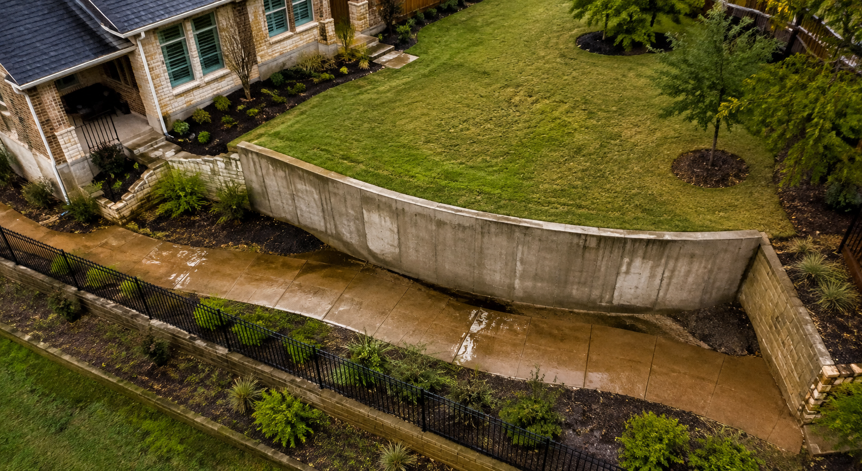Aerial view of a bowed concrete retaining wall curving toward a wet Fort Worth walkway