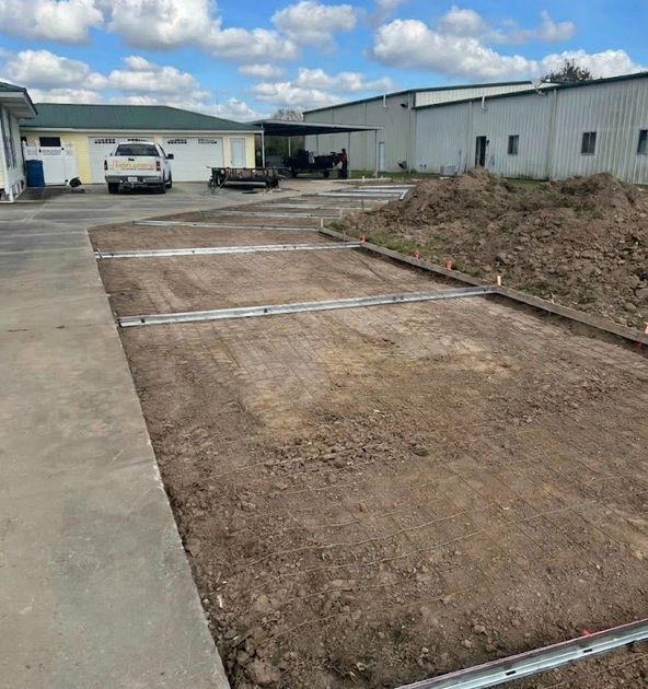 Concrete construction site in Fort Worth, TX with a dirt pad, concrete edge, and industrial buildings under a cloudy sky