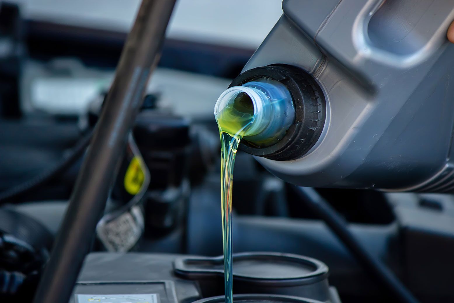 Pouring motor oil into a car engine, clear liquid, grey container, black engine components visible.