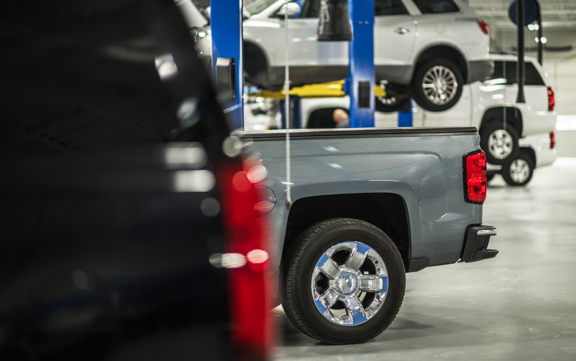 Cars parked in a bright auto repair garage, with a blue pickup in the foreground.