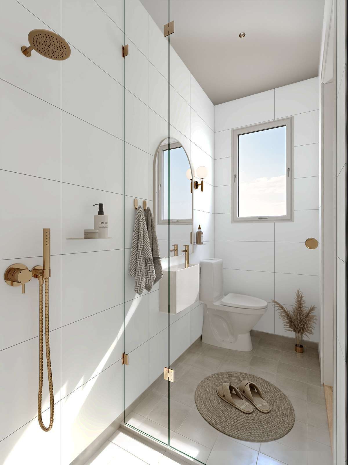 Modern white bathroom with gold fixtures, shower, toilet, and arched mirror.