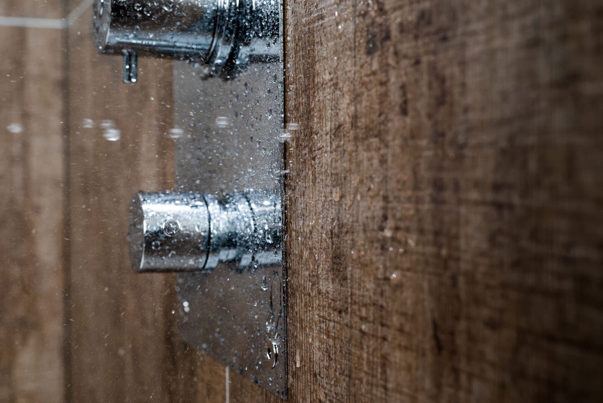 Chrome shower fixtures with water droplets against a textured brown tile wall.