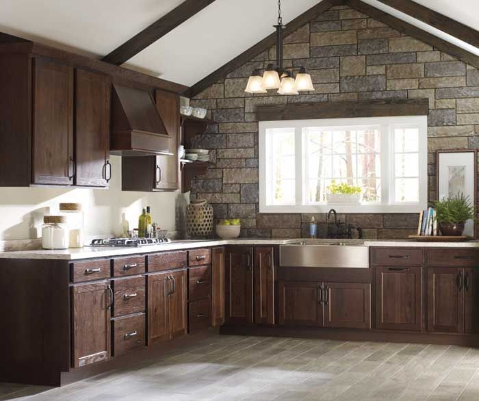 Kitchen with dark brown cabinets, stone wall, and window with sink.