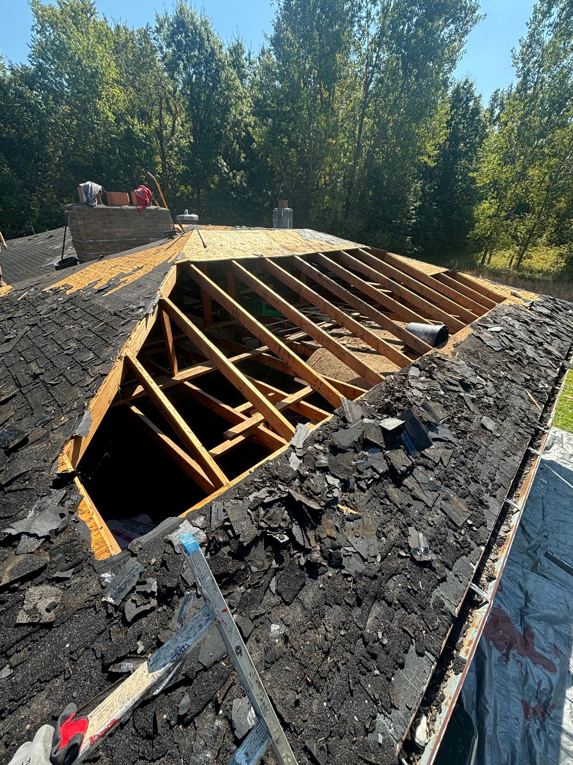 Dark gray tiled roof of a house with two skylights and a chimney against a blue sky.
