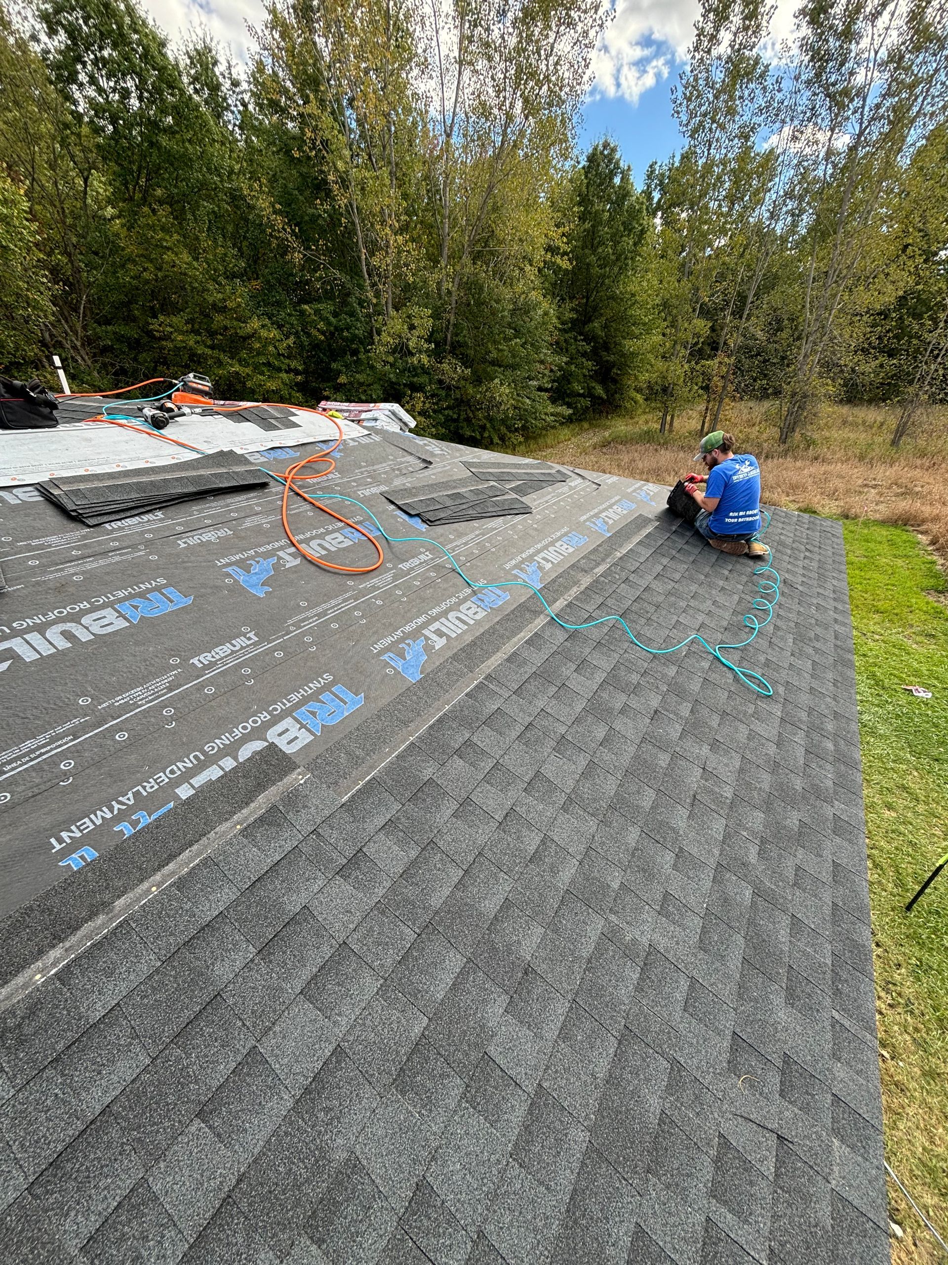 Two roofers working on a shingled roof under a sunny sky.