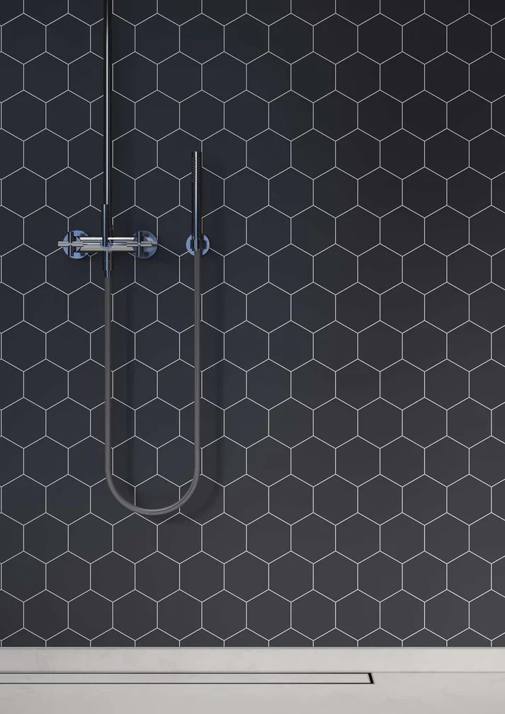 Dark hexagon-tiled shower wall with silver showerhead and handle against a white tub.