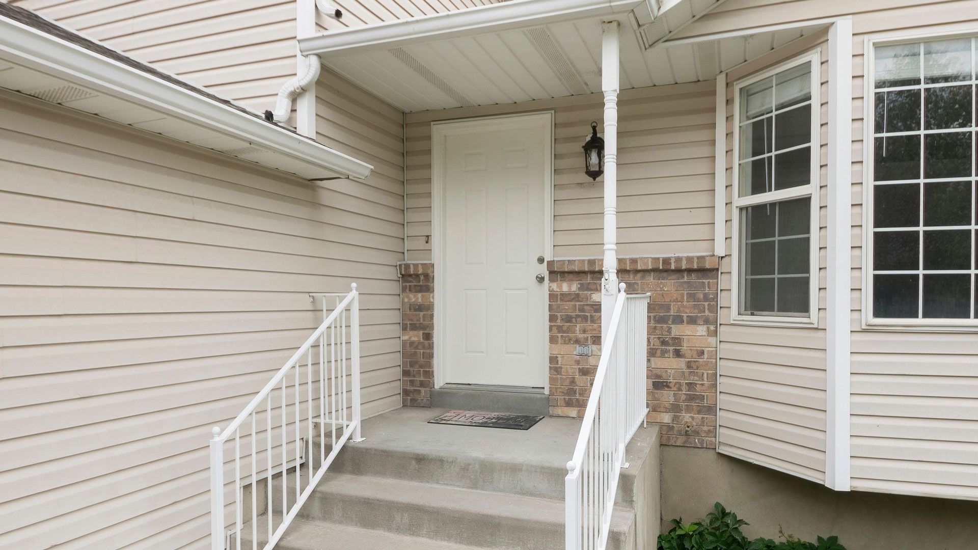 Entryway with white door, porch, brick accents, and stairs with white railing.