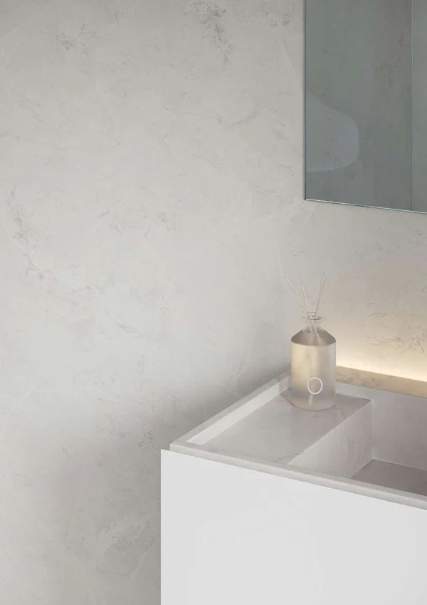 White bathroom with a minimalist design, featuring a sink, mirror, and decorative reed diffuser.