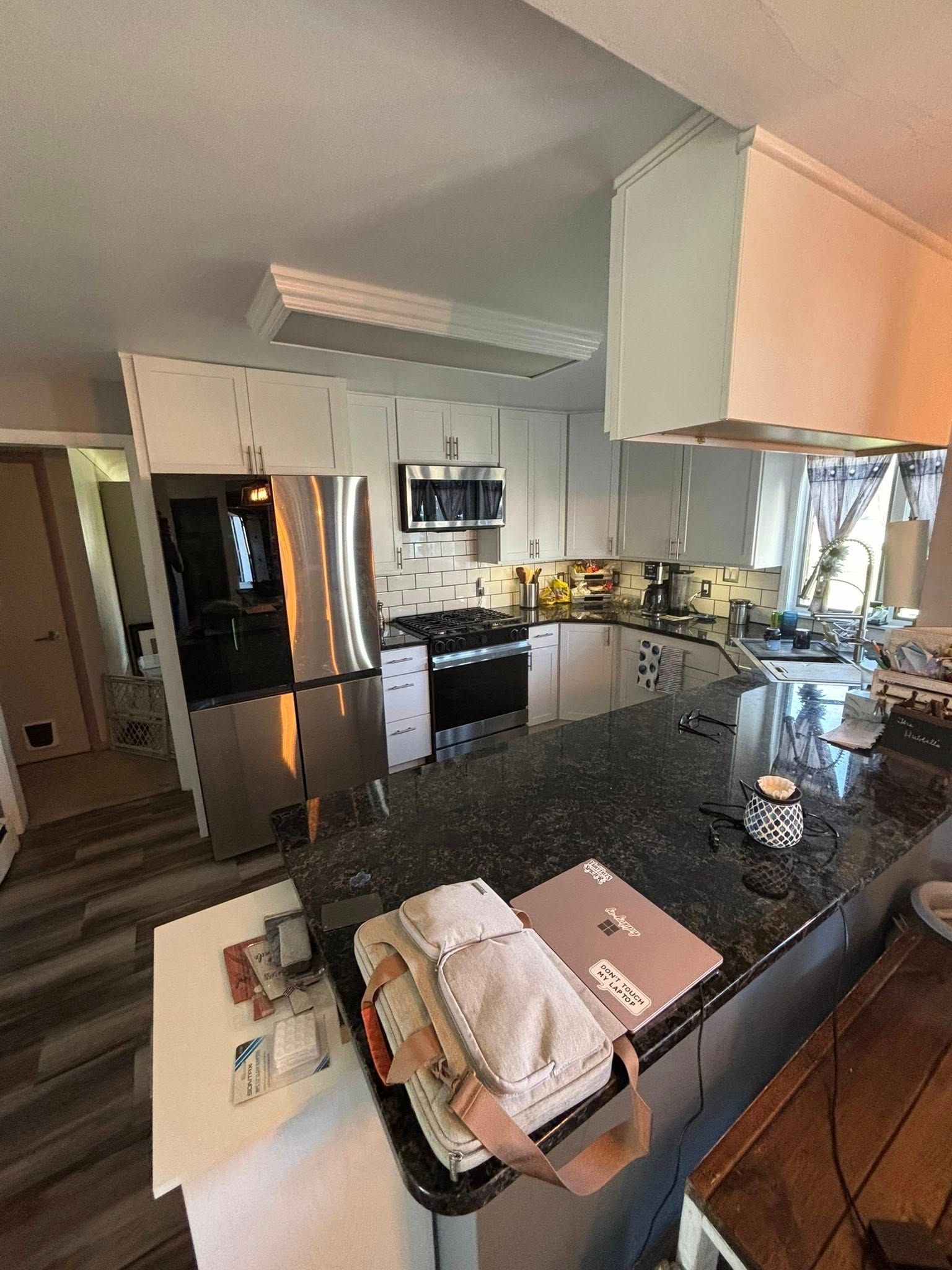 Kitchen with stainless steel appliances, dark countertops, and white cabinets. A laptop and purse are on the countertop.