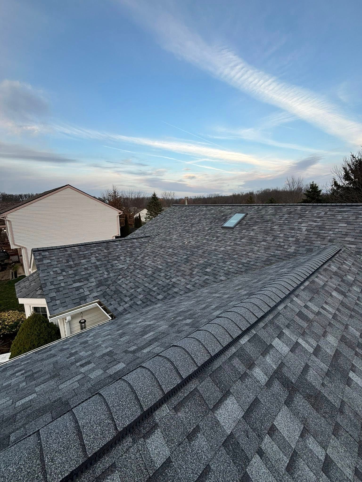 Roof with dark gray shingles against a partly cloudy blue sky.