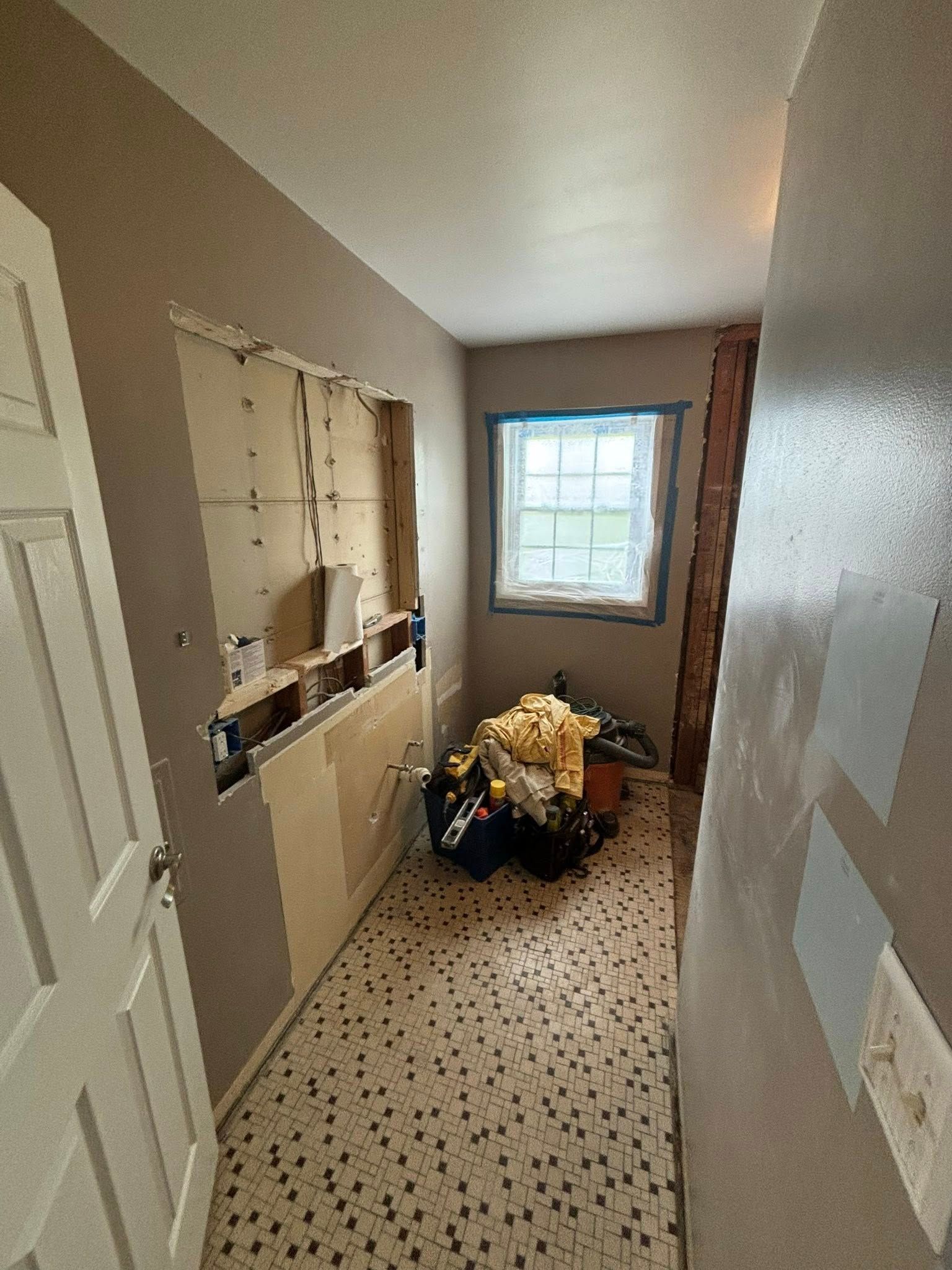 Bathroom under renovation, drywall removed exposing studs and wiring. Window visible, debris on floor.