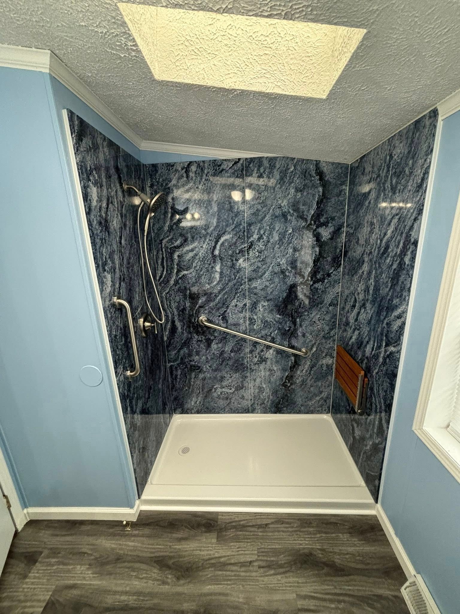 A shower with blue marble-patterned walls, a white base, and a grab bar in a bathroom with blue walls.