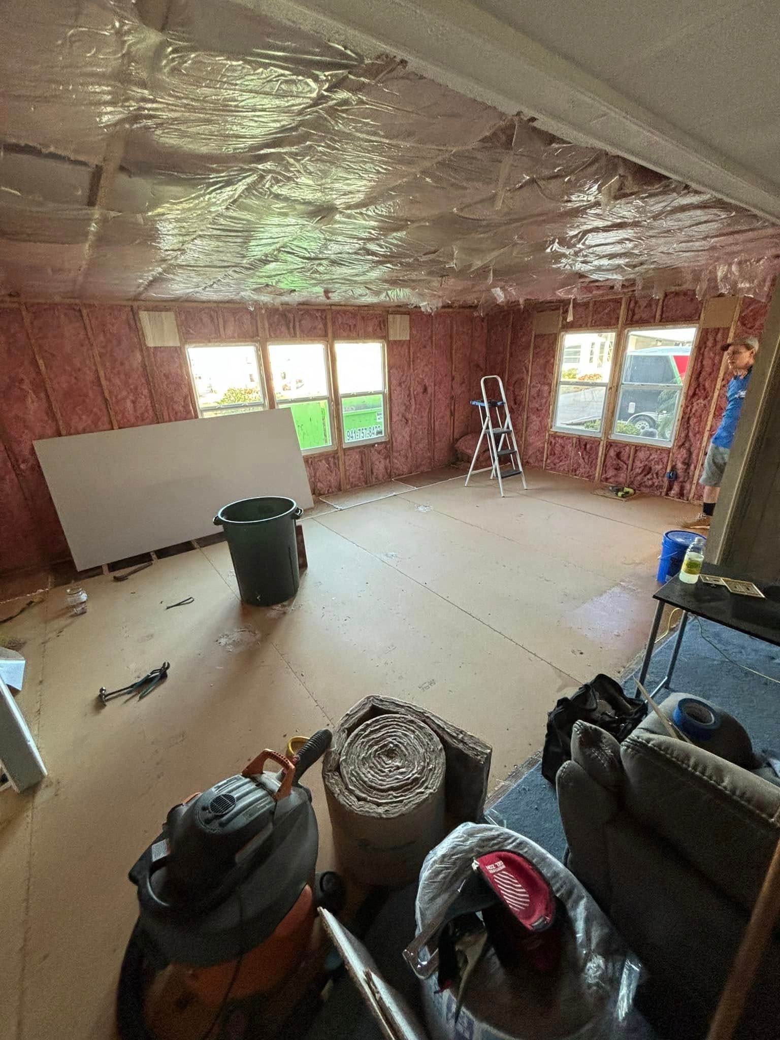 Interior of a room under construction, with pink insulation, windows, and tools on the floor.