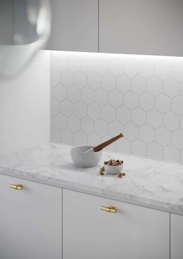 White kitchen counter with bowl, nuts, and wooden spoon against honeycomb tile backsplash.