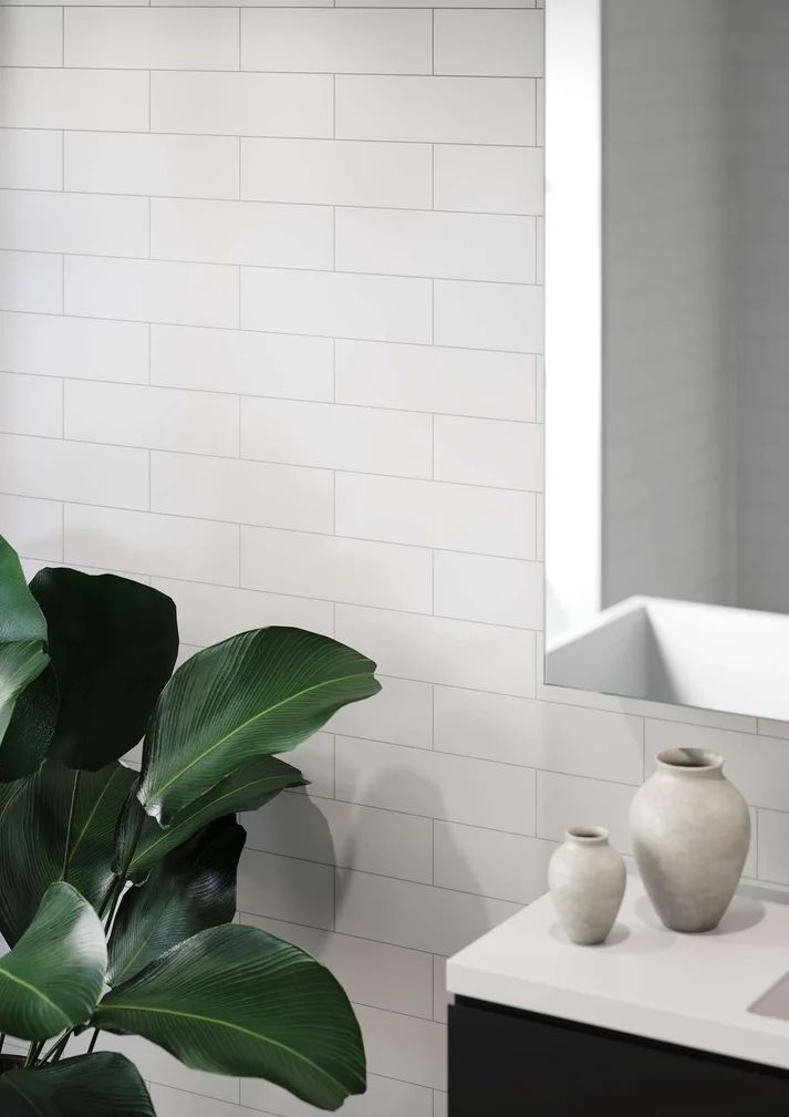 White brick-tiled wall in a bathroom, with a plant and two vases on a countertop under a mirror.