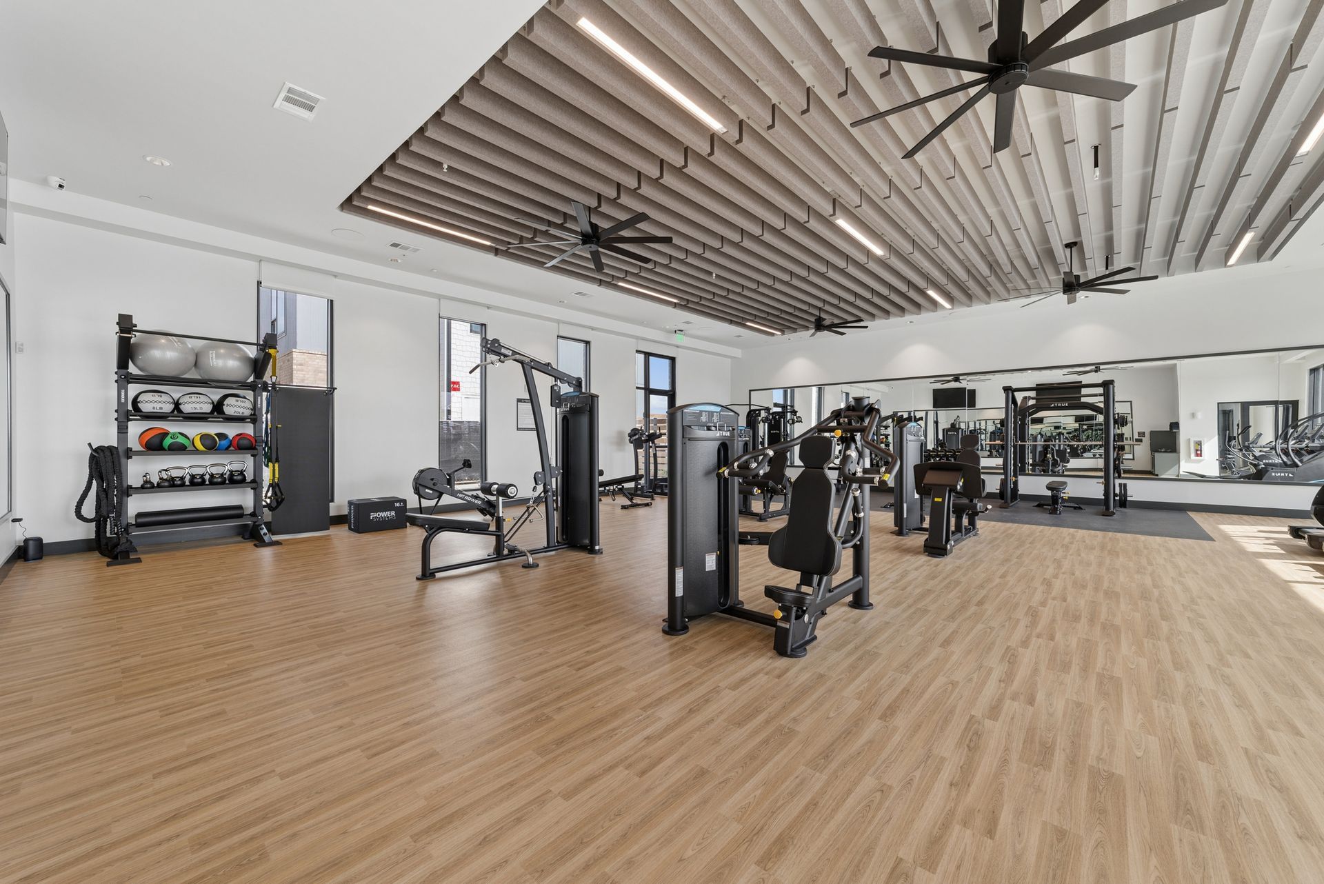 Spacious modern gym with wood floors, weight machines, treadmills, and a high ceiling with fans.