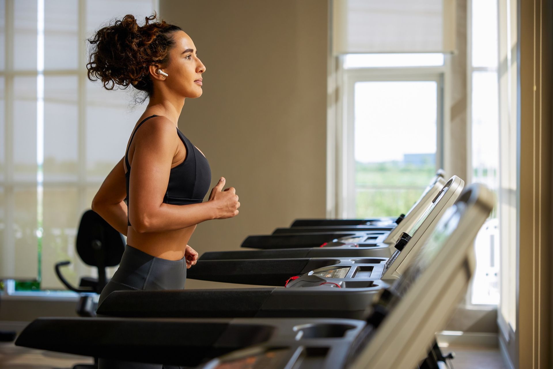 Woman walking on a treadmill in a gym, side view by large windows
