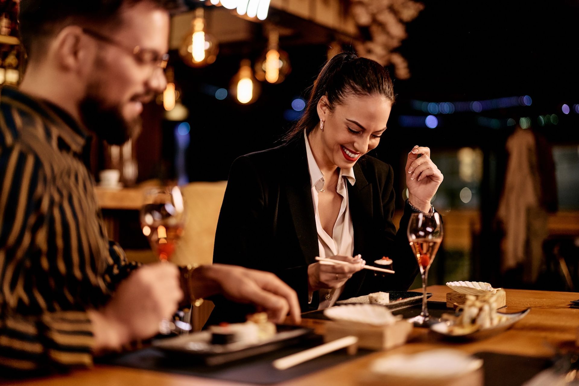 Two people dining at a warmly lit restaurant table, smiling and raising glasses over dessert