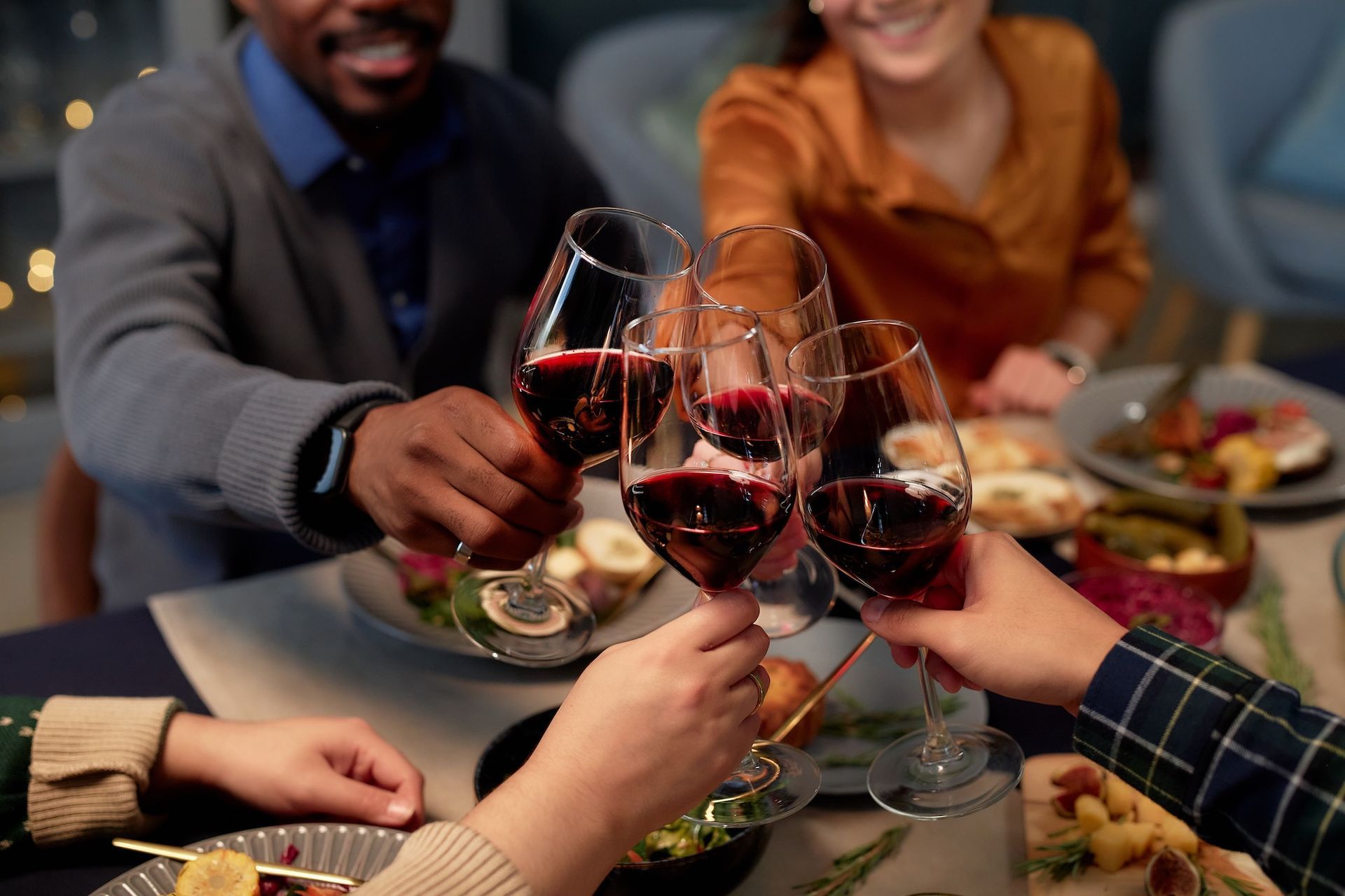Friends clinking glasses of red wine at a candlelit dinner table with plates of food