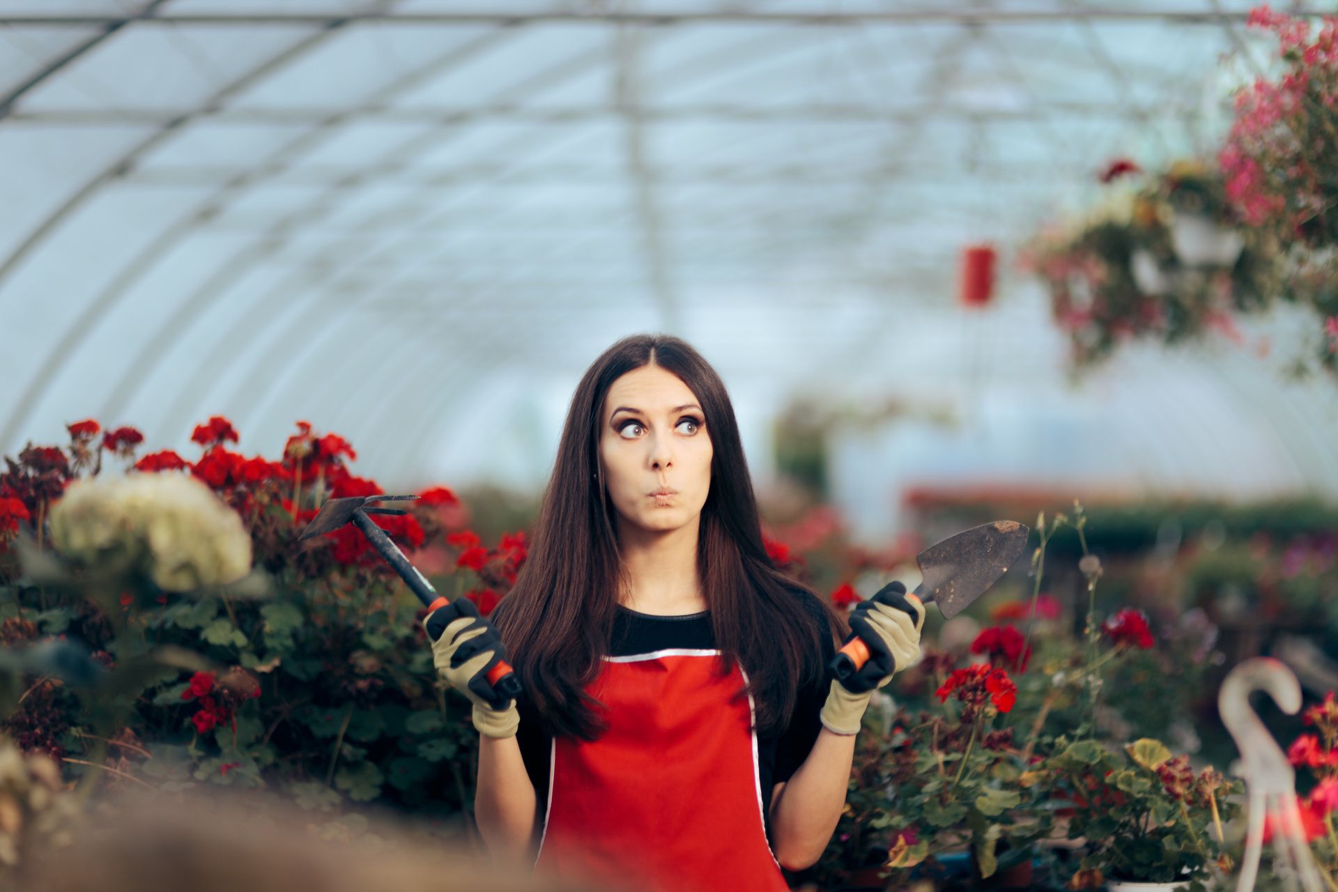 A greenhouse worker holding gardening tools with a worried look.