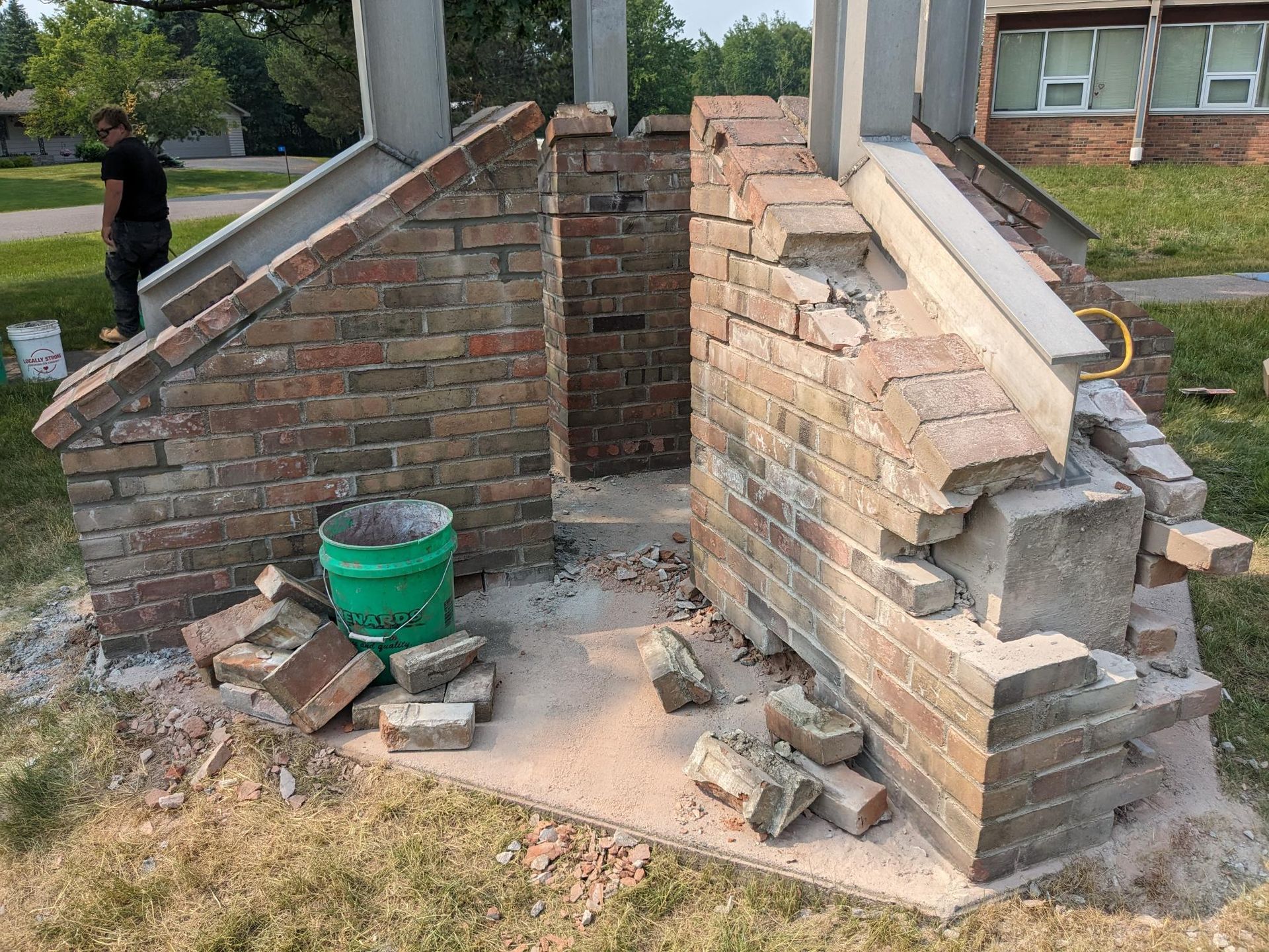 A green bucket is sitting on the ground next to a brick wall.