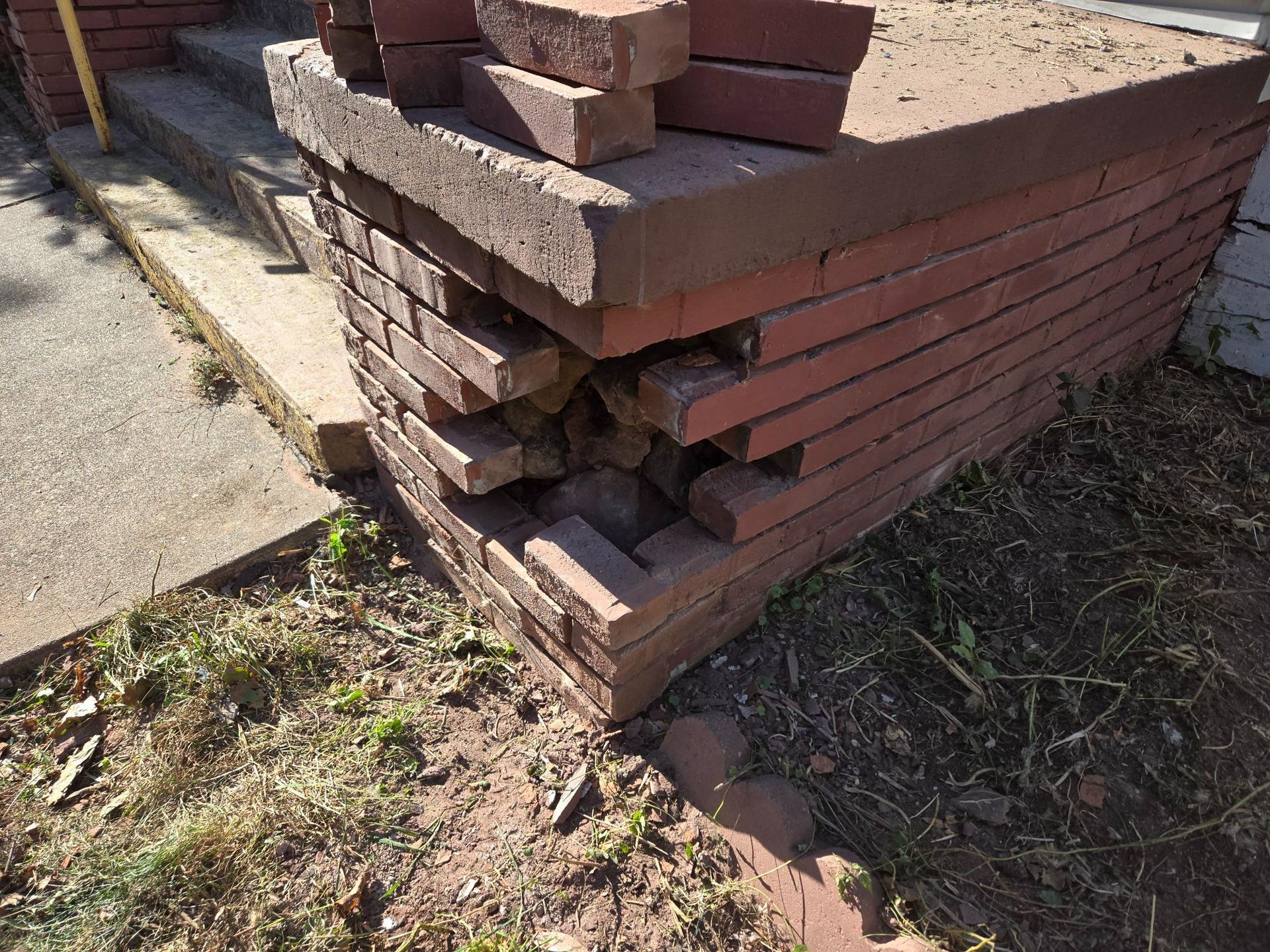 A pile of bricks is sitting on the ground next to a sidewalk.