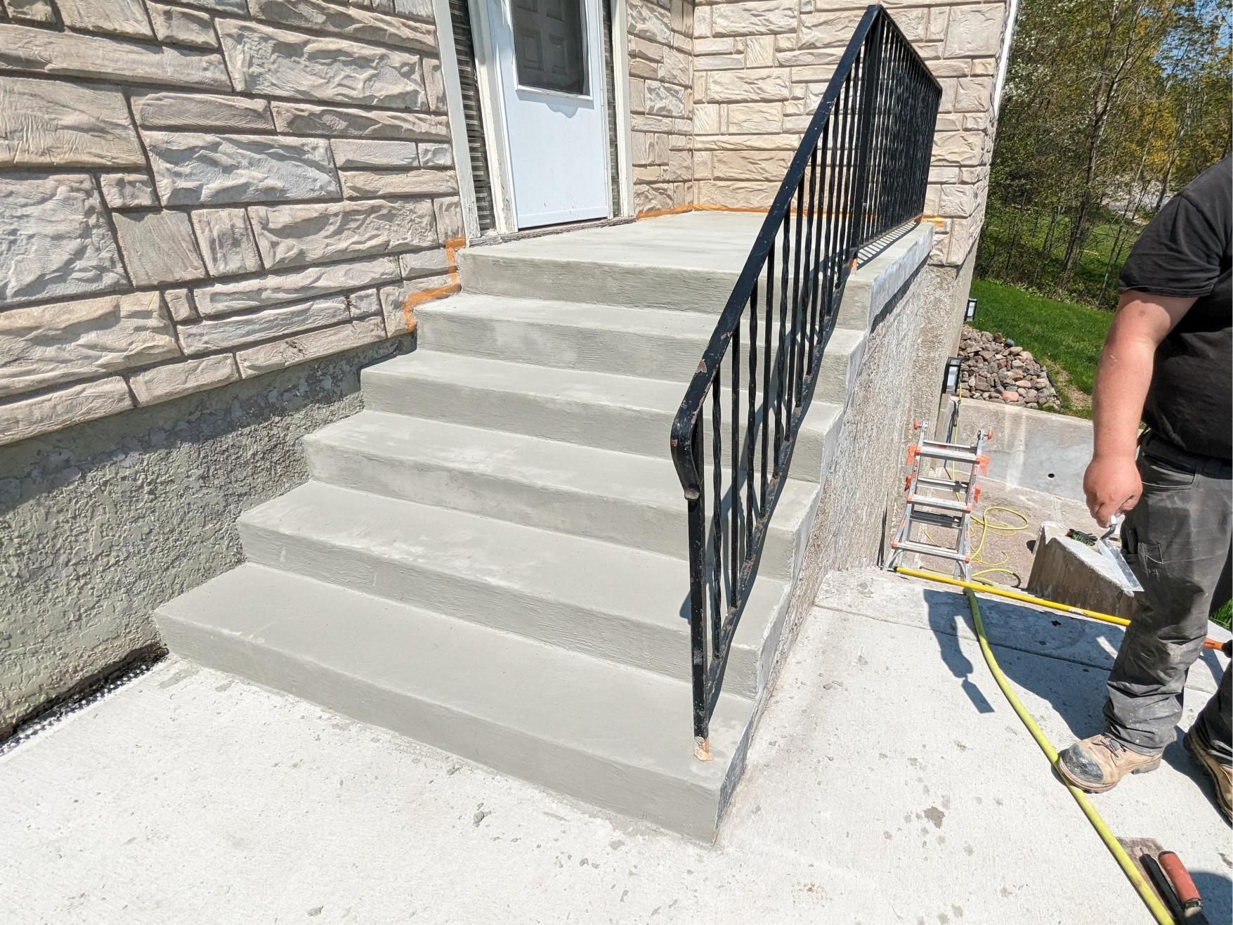 A man is measuring a concrete staircase with a metal railing.