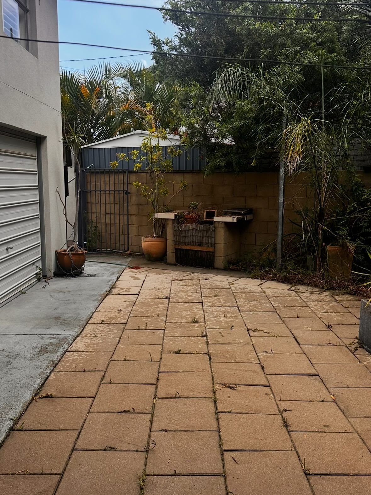 A Paved Outdoor Patio Area With a Stone Bench and Potted Plants — Coastal Pressure Solutions in Oxenford, QLD