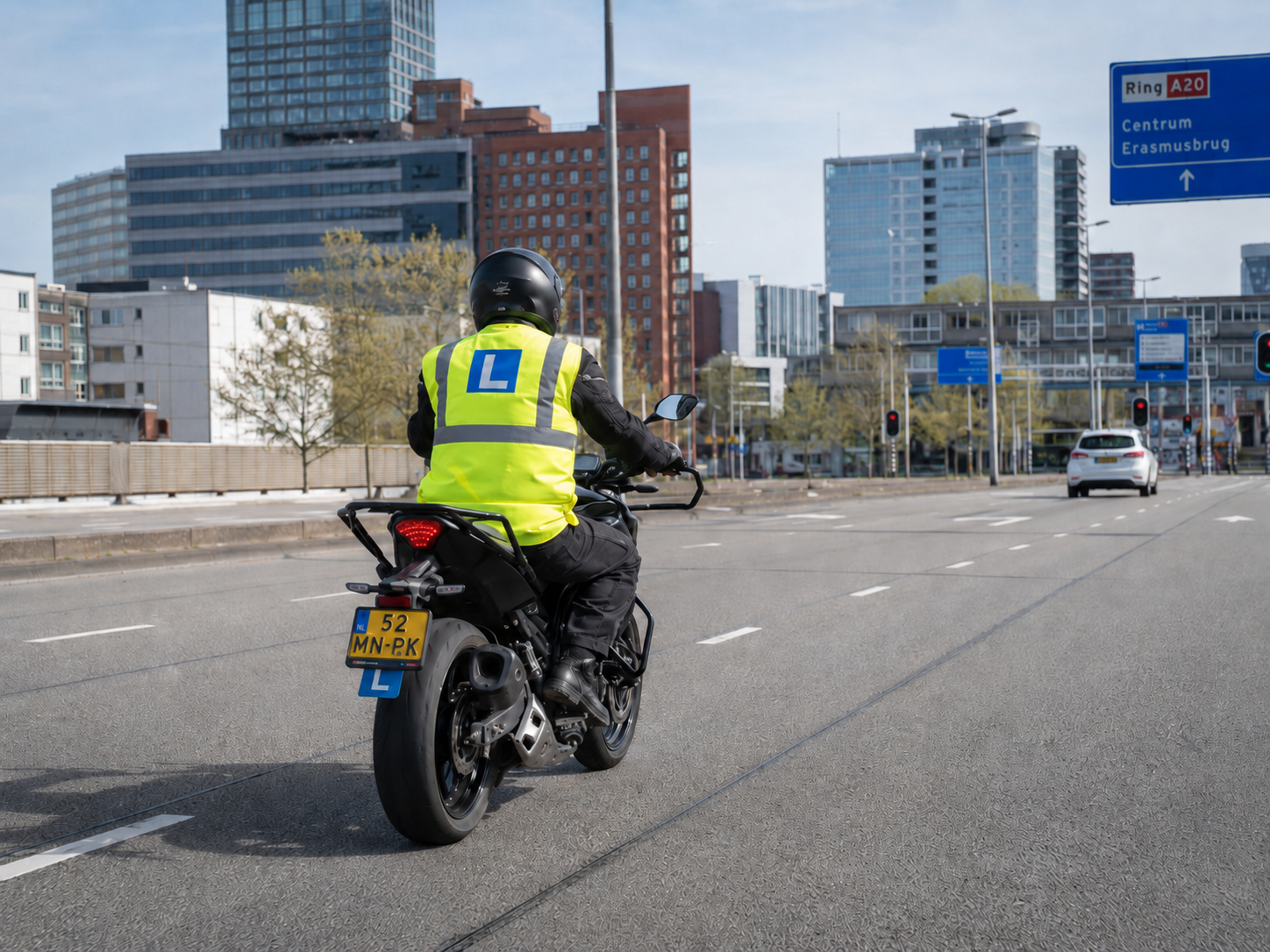 Een motorrijder in een geel reflecterend vest rijdt over een stadssnelweg met gebouwen in de verte.