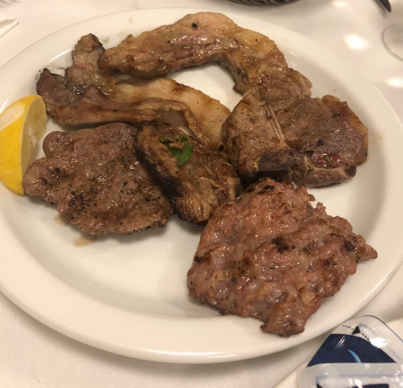 Carne alla griglia su un piatto bianco con uno spicchio di limone.