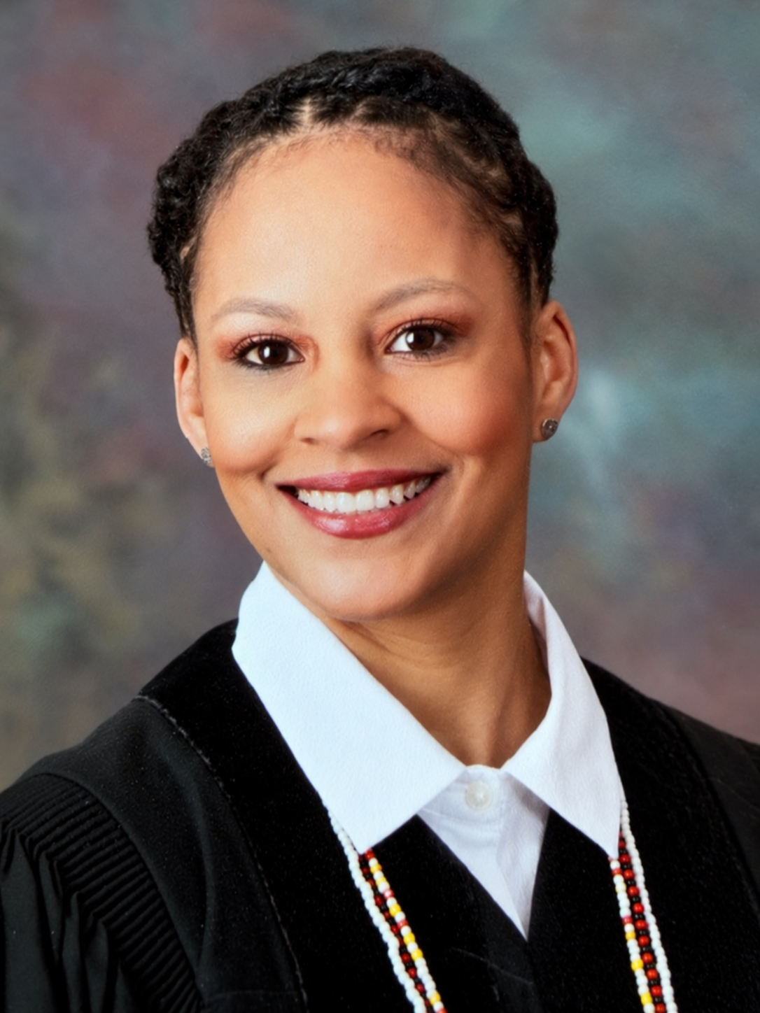 Shakira King smiling in a black jacket and white collared shirt against a gray backdrop